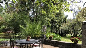 Mesa redonda con sillas y una planta en maceta en un jardín con muros de piedra y diversa vegetación.