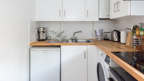 A compact kitchen with white cabinets, a dishwasher, a washing machine, and a coffee maker. - Cozy Fitzrovia studio on a quiet cobbled street in the West End! (London)
