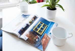 Una revista abierta sobre una mesa con una planta y dos tazas blancas.