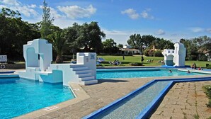 Une piscine au design géométrique blanc unique, entourée d’une allée pavée et d’une zone herbeuse où les gens se détendent.