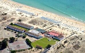 An aerial view of a coastal area with a beach, a parking lot, and several buildings including a large white structure with a red roof.