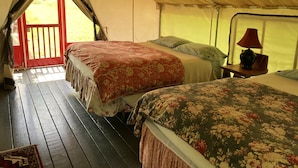 Un hébergement sous tente comprenant deux lits, une petite table avec une lampe et une vue sur l’extérieur par une porte.