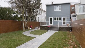 Ein Wohngarten mit einem gepflasterten Weg, einem Holzzaun und einem grauen Haus.
