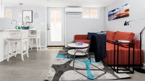 Ein modernes Wohnzimmer mit einem roten Sofa, einem weißen Essbereich mit Küchenzeile und einem großen Fenster mit Jalousien.
