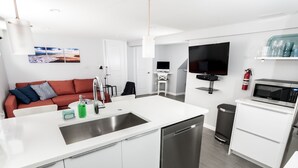 Eine moderne Küche mit Geschirrspüler, Mikrowelle und Fernseher. Es gibt eine Couch mit Kissen und einen kleinen Tisch mit Lampe.