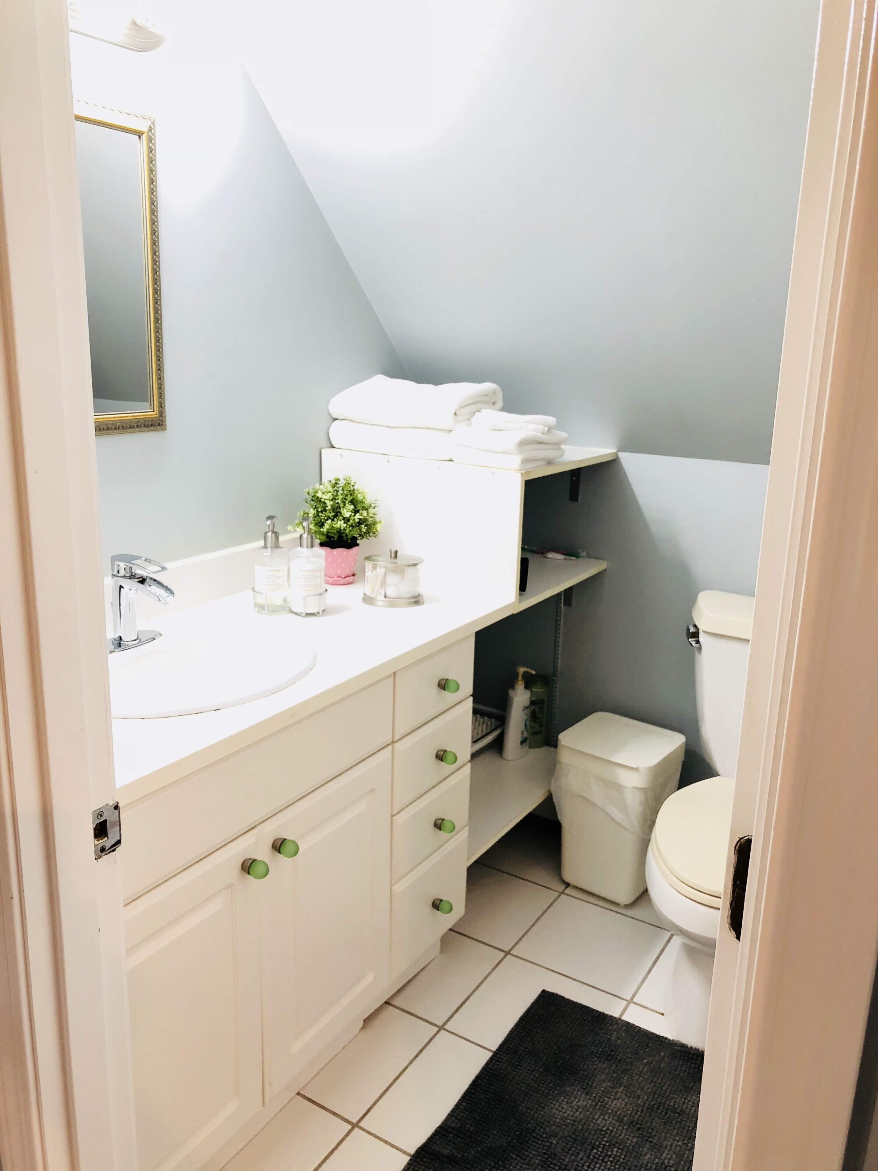 A bathroom with a white vanity, a sink, a mirror, a toilet, and a small shelf with towels.