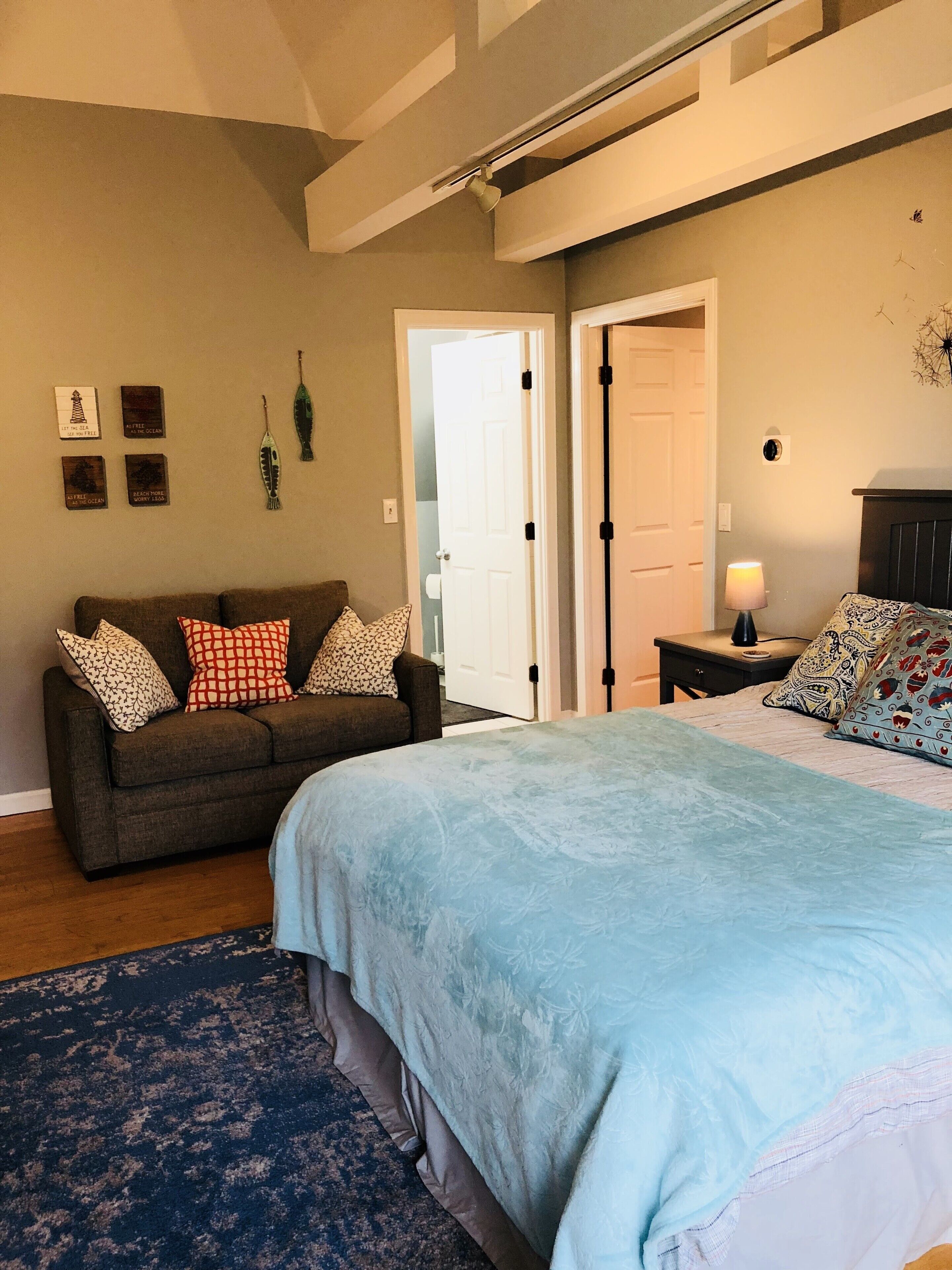 A bedroom with a bed, a sofa, a nightstand, and a door.