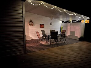 Eine überdachte Terrasse mit Esstisch und Stühlen, Lichterketten und Deckenventilator.