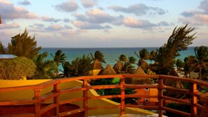 Vista de un resort con valla de madera, palmeras y una playa al fondo.