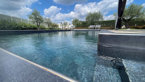 A swimming pool with clear water, surrounded by a landscaped area with trees and a few lounge chairs. - Exclusive Tuscan Villa with Black Pool & Jacuzzi (Altopascio)