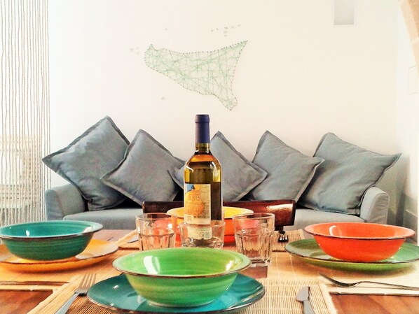 A dining table with various bowls and glasses, a bottle of wine, and a sofa with cushions in the background. - House Maier center Trapani (trapani)