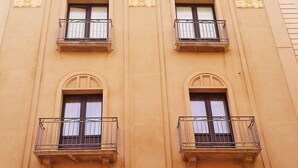 Ein Gebäude mit drei Fenstern, jedes mit einem Balkon. Die Fassade ist schlicht, jedoch mit dekorativen Fensterrahmen.
