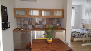 A compact kitchen with a wooden countertop, stainless steel appliances, and a colorful tile backsplash.