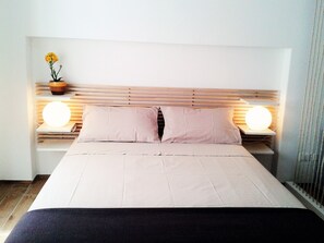 A neatly made bed with a wooden headboard, two bedside tables with round lamps, and a vase with flowers on one table. - House Maier center Trapani (trapani)