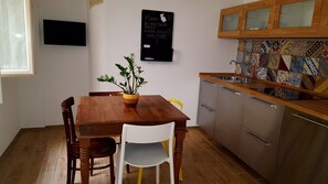 A dining area with a wooden table, white chairs, a potted plant, a blackboard with writing, and a kitchen with a patterned backsplash. - House Maier center Trapani (trapani)