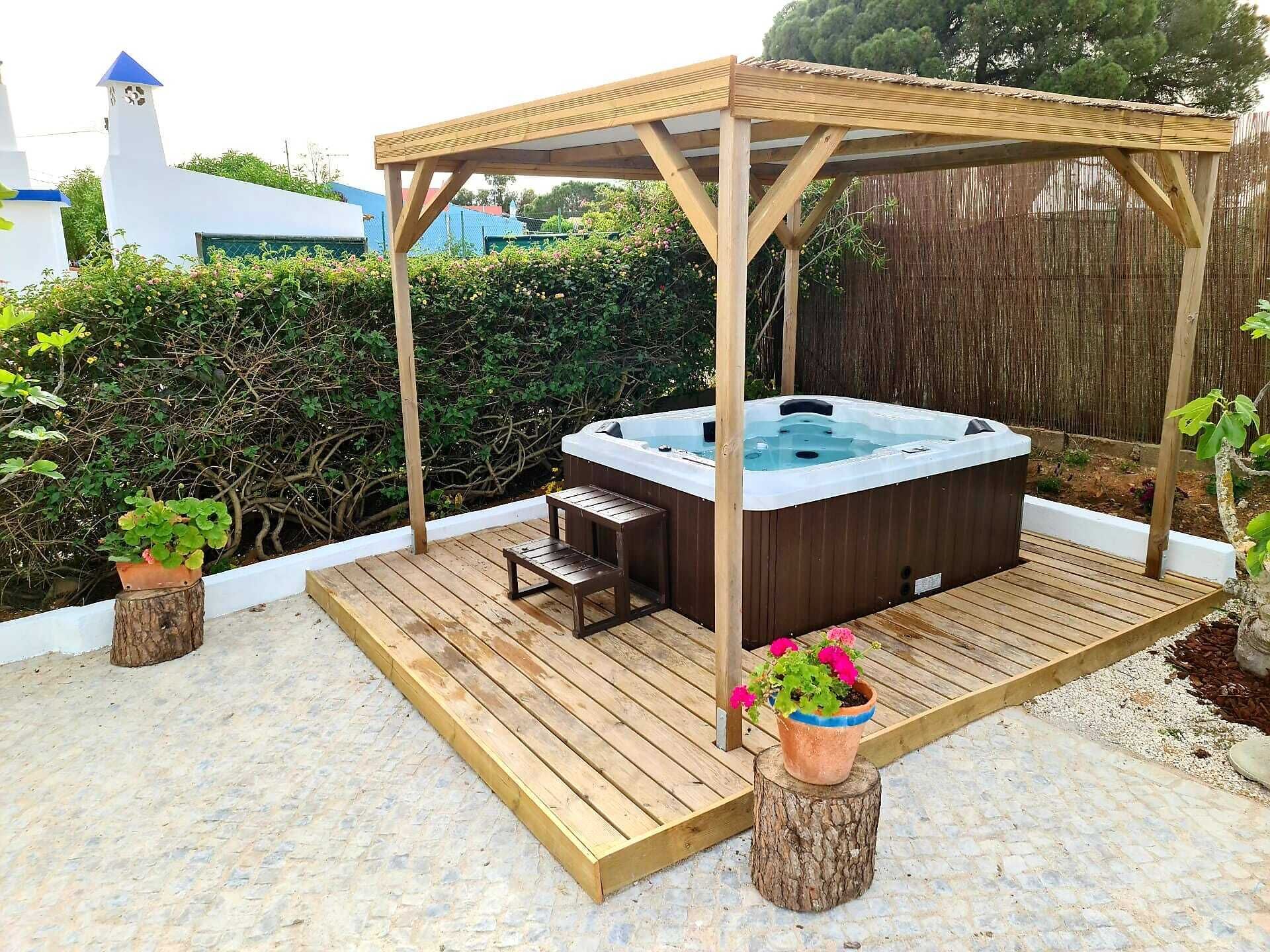 Ein Whirlpool unter einer Holzw pergola auf einer Holzterrasse mit Kübelpflanzen.