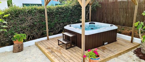 A hot tub under a wooden pergola on a wooden deck with potted plants.