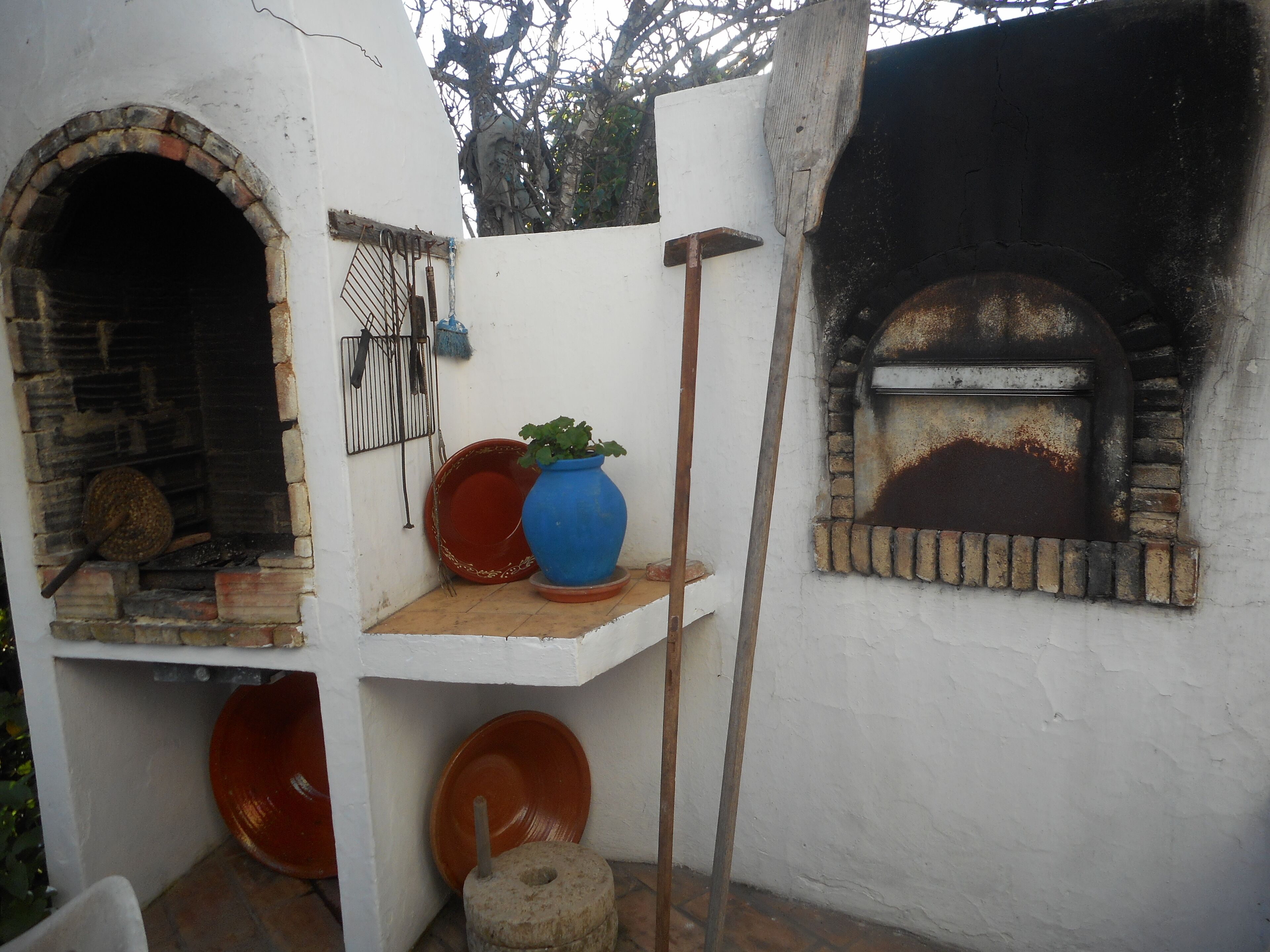 Een rustieke buitenkeuken met een bakoven, een grote blauwe pot en een bord rood op een plank.