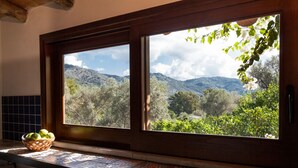 A kitchen with a large window overlooking a mountainous landscape, a woven basket with fruit on the counter, and a tiled backsplash. - Farm holidays with pool in Sicily, among the Nebrodi's park and close to the sea (Rocca di Capri Leone)