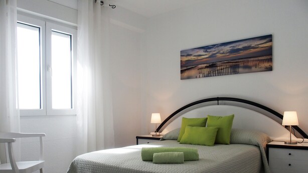 A bedroom with a bed, two bedside tables, a chair, a window, and a painting on the wall. - Apartment/ flat - AyamonteResidential flat (Ayamonte)