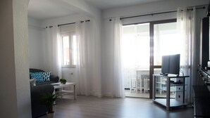 A modern living room with a sofa, a coffee table, and a TV on a stand. There is a sliding glass door leading to a balcony. - Apartment/ flat - AyamonteResidential flat (Ayamonte)