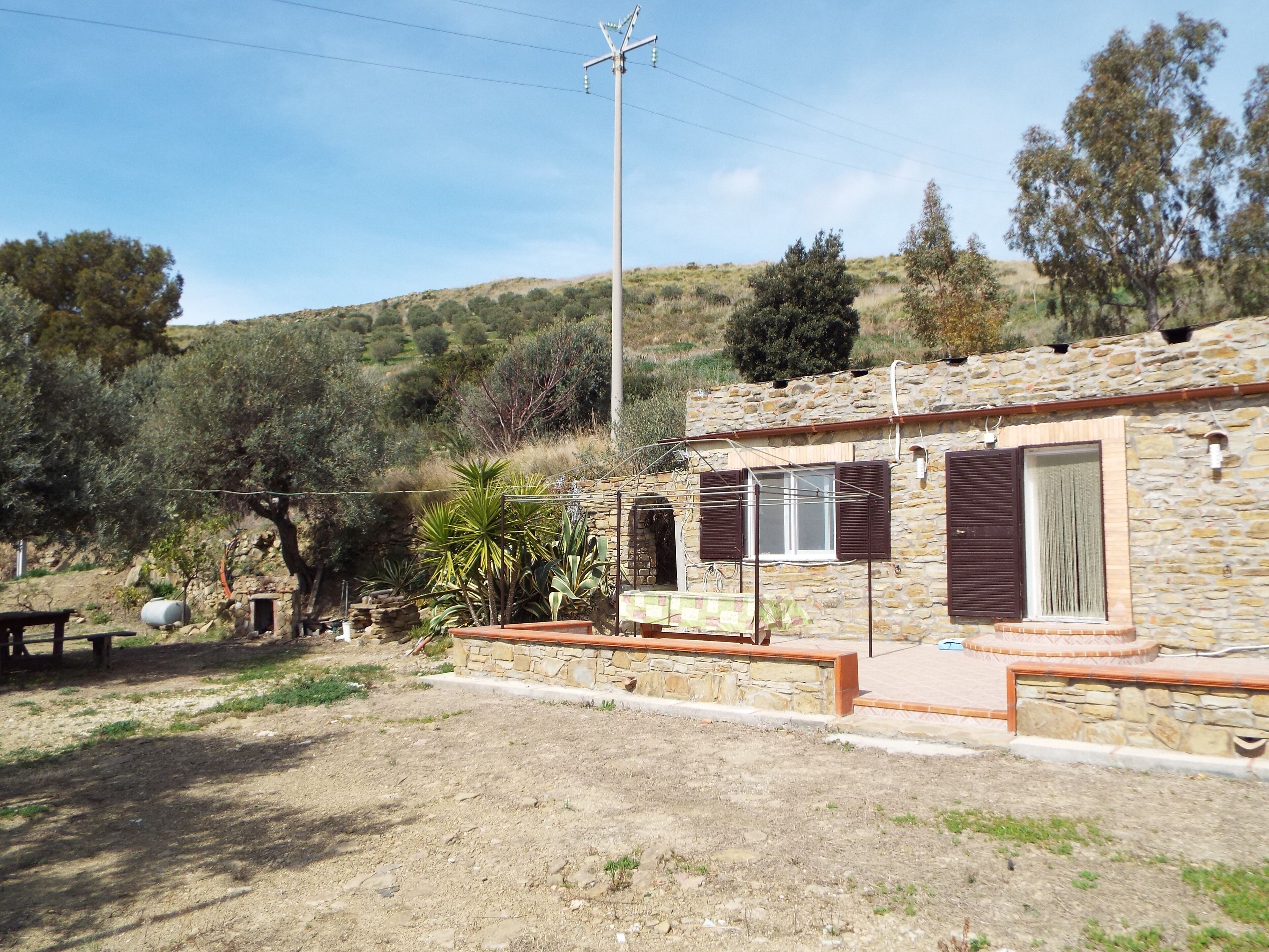 A stone house with a patio, a stone wall, and a view of a hillside.