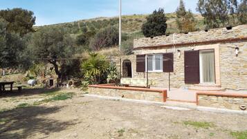 A stone house with a patio, a stone wall, and a view of a hillside.