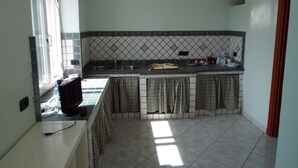 Une cuisine avec un mur recouvert de carreaux, une fenêtre et un luminaire suspendu.