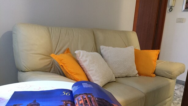A beige sofa with orange and white cushions, a magazine with a building image, and a marble floor. - Rome: Apartment/ flat - Roma (Roma)