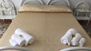 A neatly made bed with a beige bedspread, two rolled white towels with gold flowers, and a white lamp on a bedside table. - Rome: Apartment/ flat - Roma (Roma)