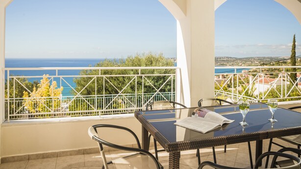 Un balcón con vista al mar, una mesa con dos vasos y una silla.