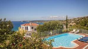 Piscina con sillas de descanso, rodeada de vegetación y con vistas al mar.