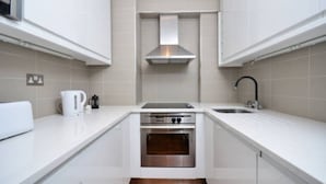 Une cuisine compacte avec des meubles blancs, un four encastré, une plaque de cuisson et une hotte en acier inoxydable.