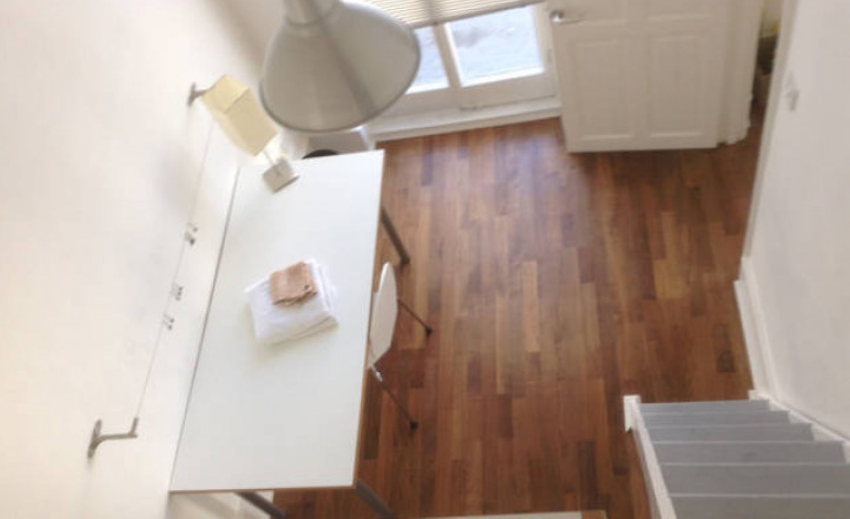 A room with a wooden floor, a white table with a towel, and a window with blinds.