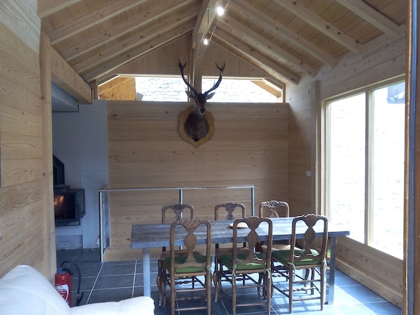 Un intérieur en bois avec un plafond haut, une tête de cerf accrochée au mur, une table à manger avec des chaises et une cheminée.