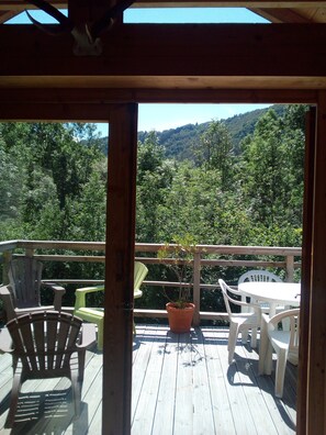 Um deck de madeira com mobiliário de exterior, incluindo cadeiras e uma mesa, com vista para uma encosta arborizada.