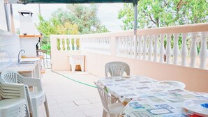 Um pátio externo com mesa de jantar, cadeiras, uma mesa pequena e uma churrasqueira.