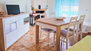 Uma cozinha compacta com área de refeições, uma televisão sobre um móvel e uma janela com cortinas azuis.