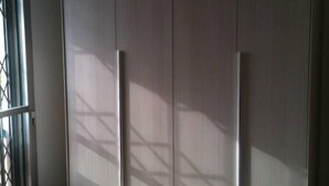 Ein Zimmer mit großem Kleiderschrank, einem gemusterten Teppich und einem Fenster mit Metallgitter.