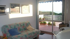 Ein Zimmer mit einer Couch, einem Tisch und einem Balkon mit Blumentöpfen.