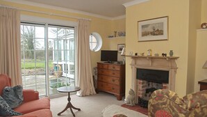 Ein Wohnzimmer mit Sofa, Sessel, Kamin, Fernseher und Blick durch eine Glastür.