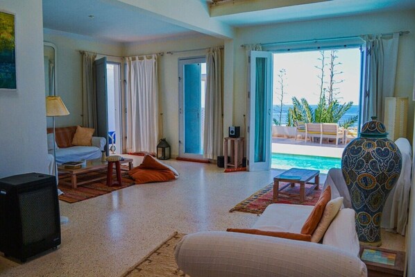 A living room with a sofa, coffee table, and a TV. There is a view of a pool and outdoor furniture through an open door.