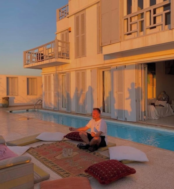A man sitting by a pool with a view of a building with balconies and sliding doors.