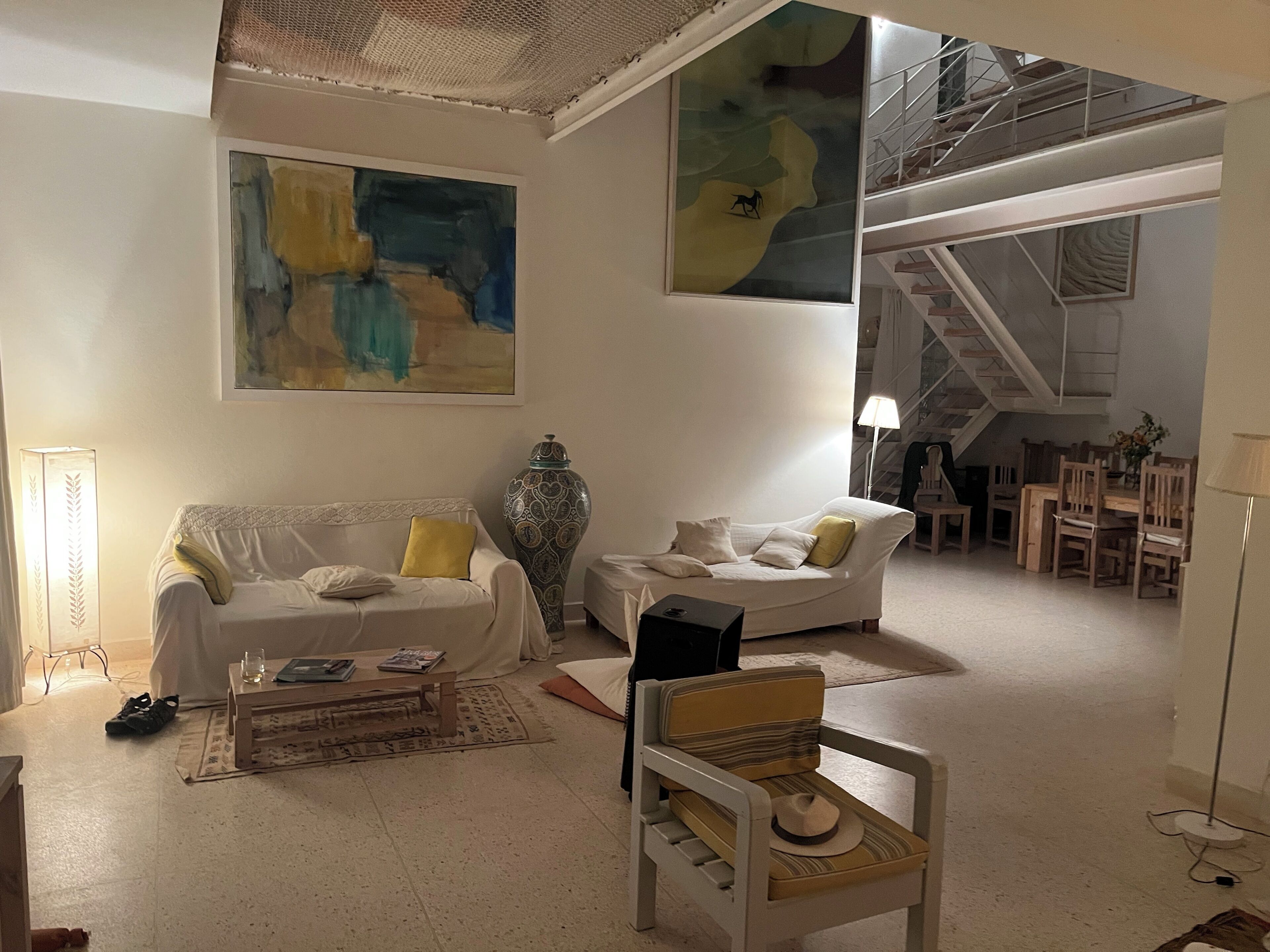 A spacious living area with two white sofas, a patterned vase, a small table with books, and a chair with a hat.