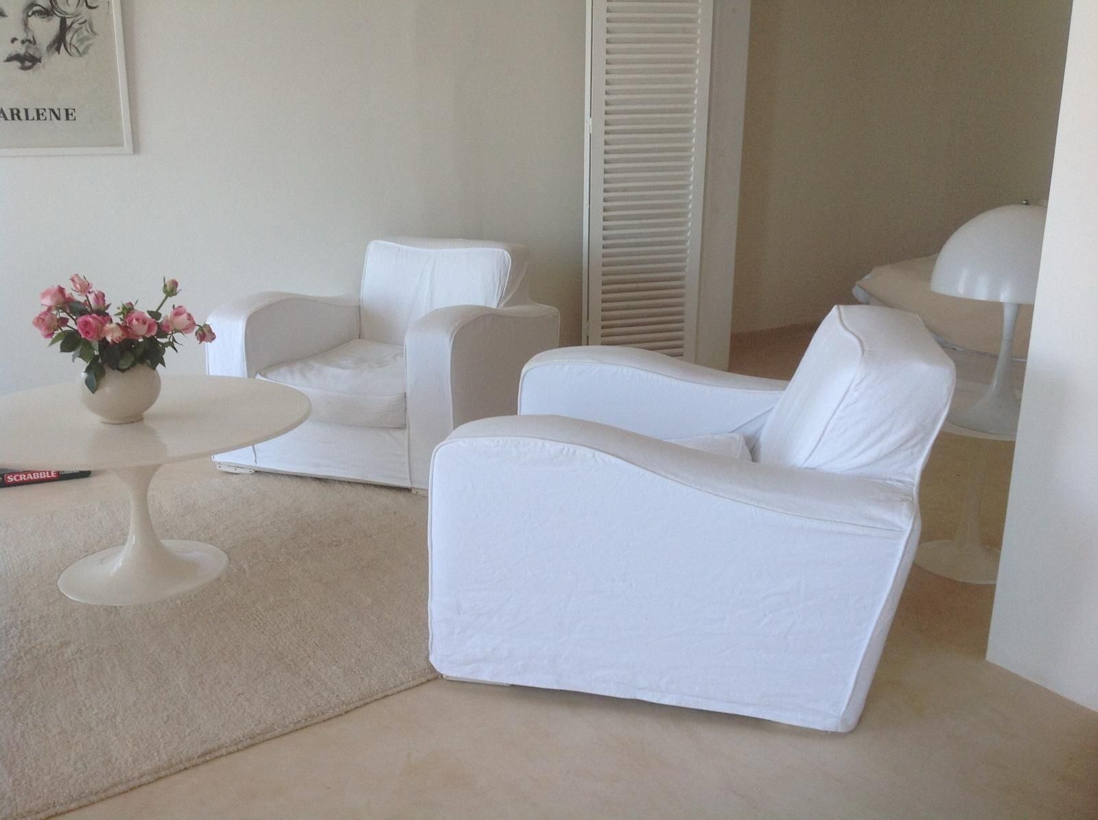 A room with two white sofas, a small round table with a vase of flowers, and a white lamp.