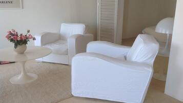 A room with two white sofas, a small round table with a vase of flowers, and a white lamp.