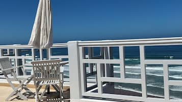 A seaside terrace with white railings, a white umbrella, and a chair.