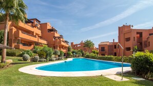 Une piscine entourée de pelouses bien entretenues et de palmiers, avec des immeubles à plusieurs étages en arrière-plan.
