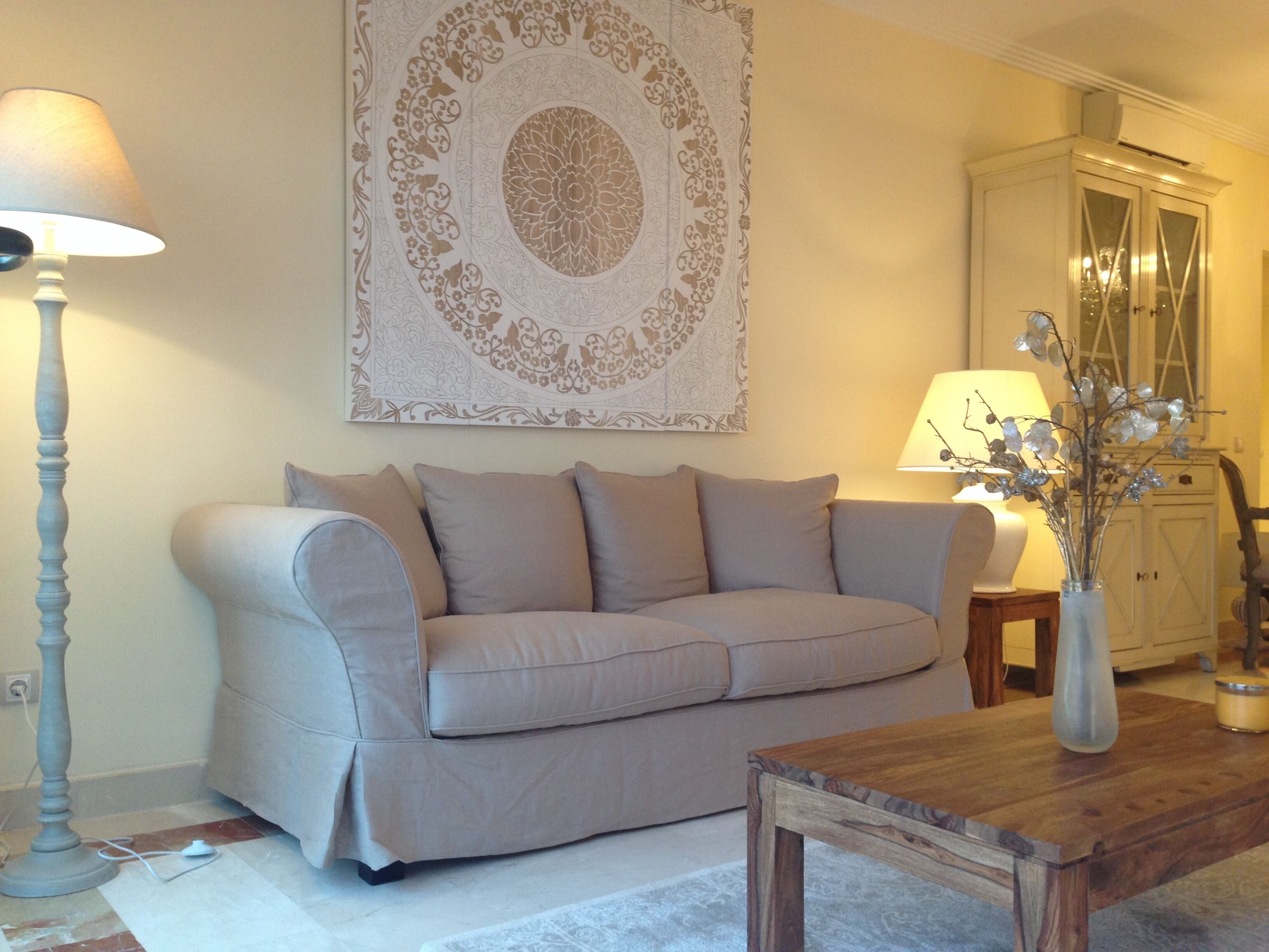 Ein Wohnzimmer mit einem beigefarbenen Sofa, einem Holztisch, einer Stehlampe und einem Wanddekor.