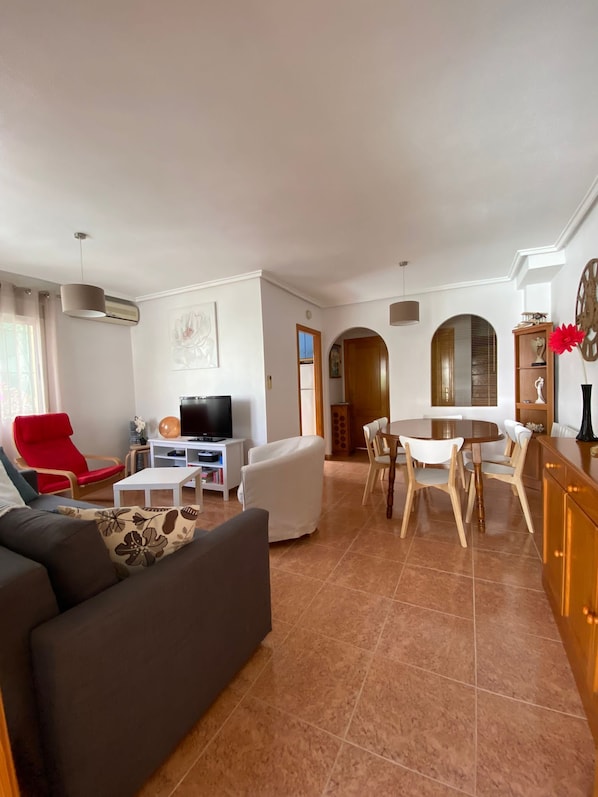 Una sala de estar con sofá, sillón rojo, televisor y un comedor con mesa y sillas.